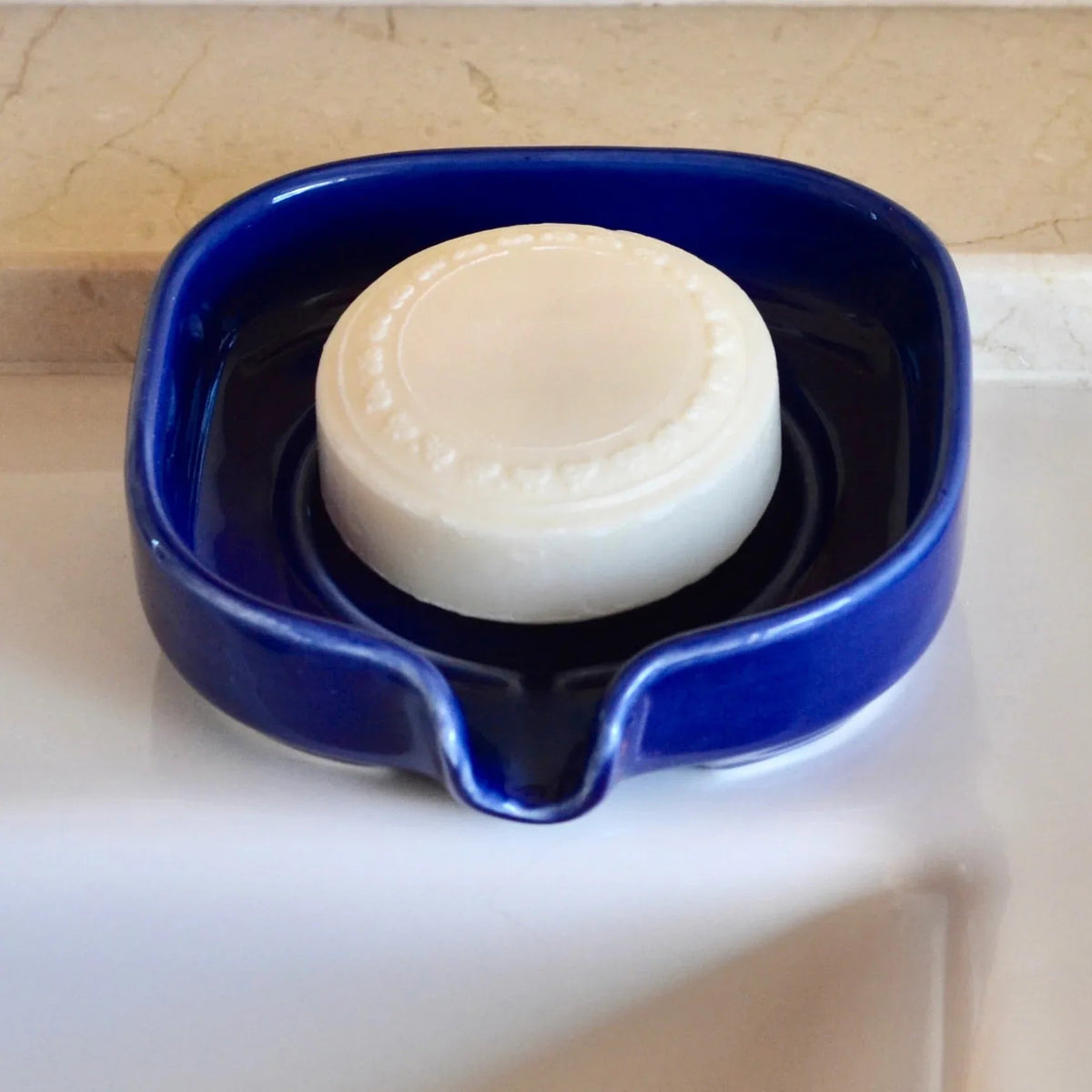 Close-up of glossy white ceramic soap dish showing water droplets draining away.