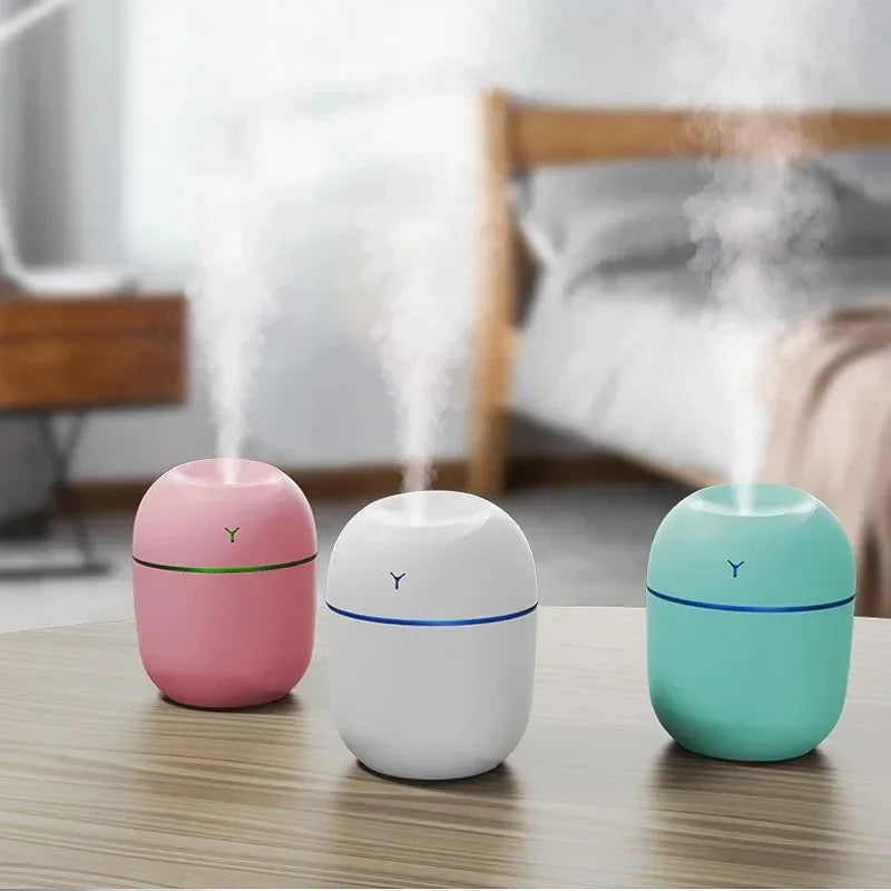 Portable ultrasonic humidifier and essential oil diffuser with LED light on wooden desk next to small plant.