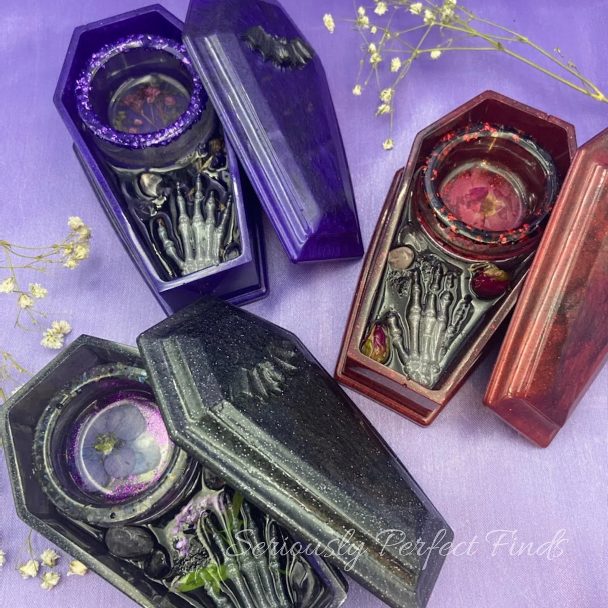 Resin coffin-shaped tealight candle holder with embedded rose quartz, dried flowers, and a skeleton hand design.