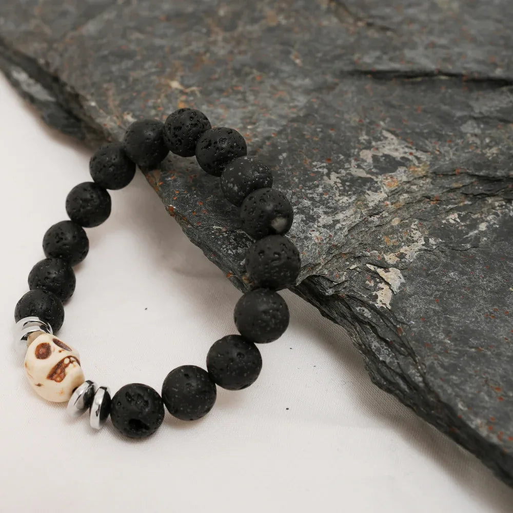 Black lava stone bracelet with silver skull bead and spacers laid out on white background