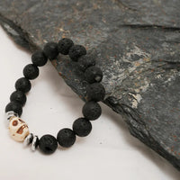 Black lava stone bracelet with silver skull bead and spacers laid out on white background