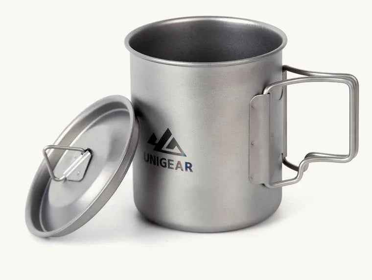 Lightweight titanium camping cup with folding handles, 450ml capacity, placed on a wooden outdoor table.