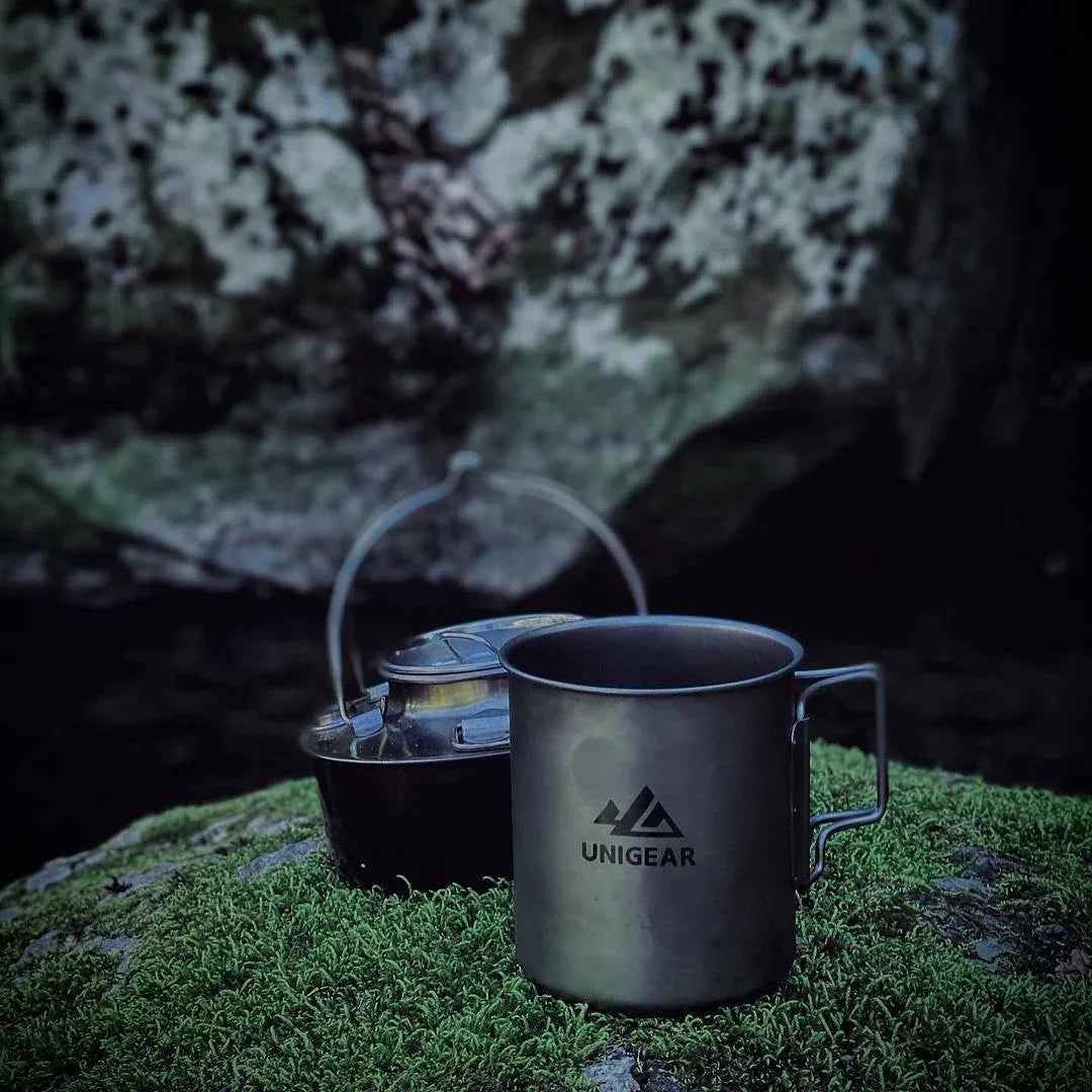 A lightweight, gray titanium camping cup with folding handles, holding up to 450ml, set on a plain surface.