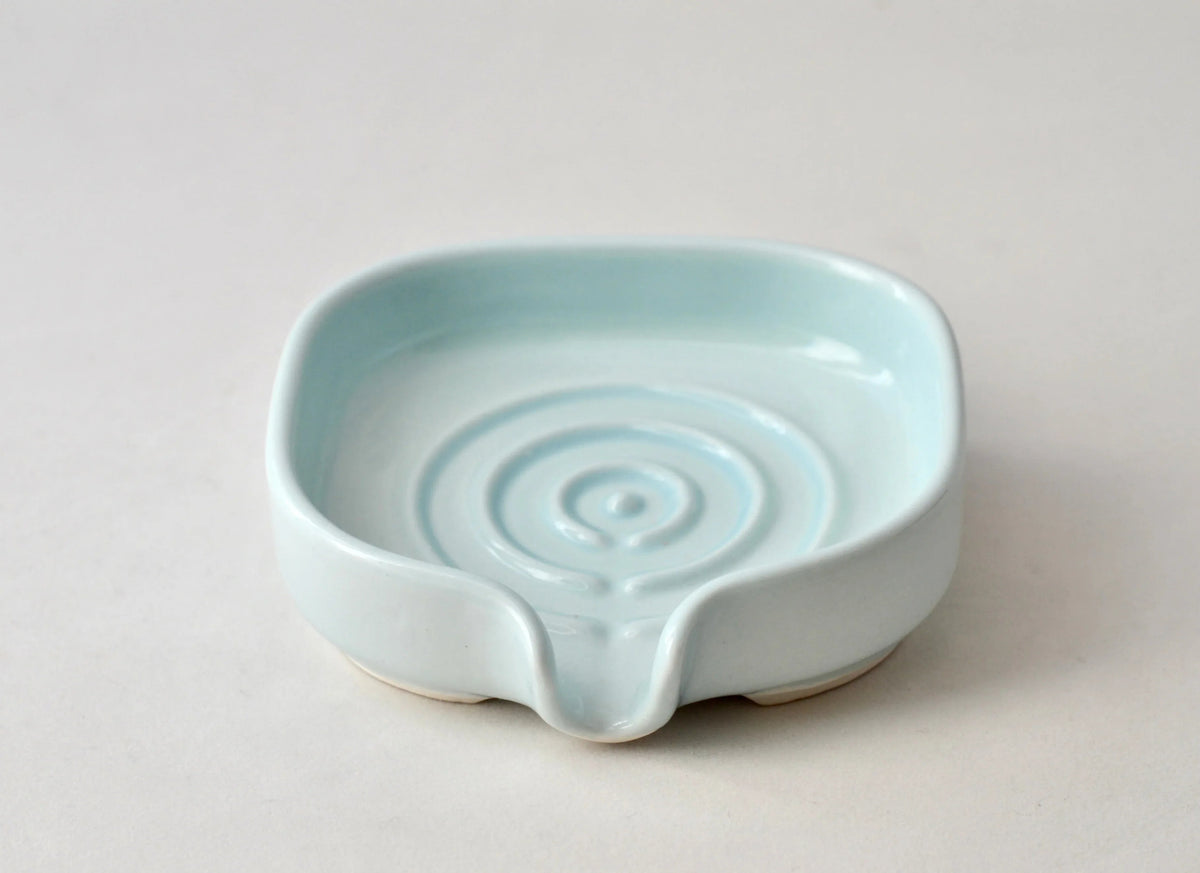 Angled view of durable porcelain soap dish with sleek curved edges.