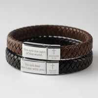 Christian bracelet worn on wrist featuring woven leather band and personalized Bible quote on metal plate.