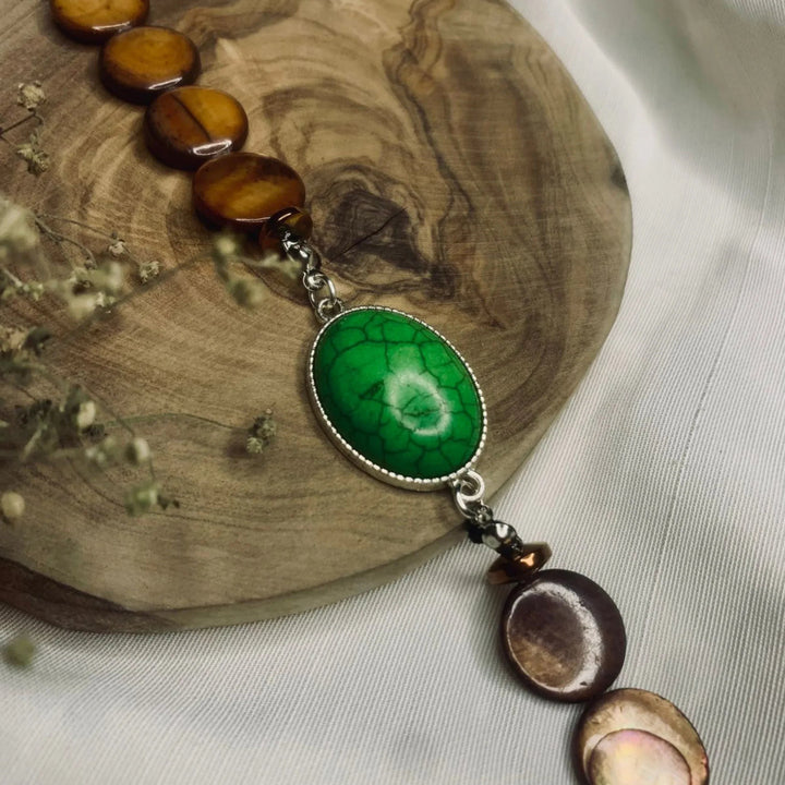 Close-up of handmade bracelet with green turquoise stone and brown beads on metal links.