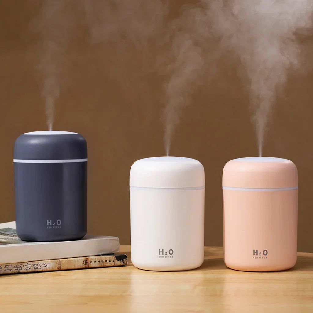 Portable air humidifier emitting mist on wooden surface with green plant in background.
