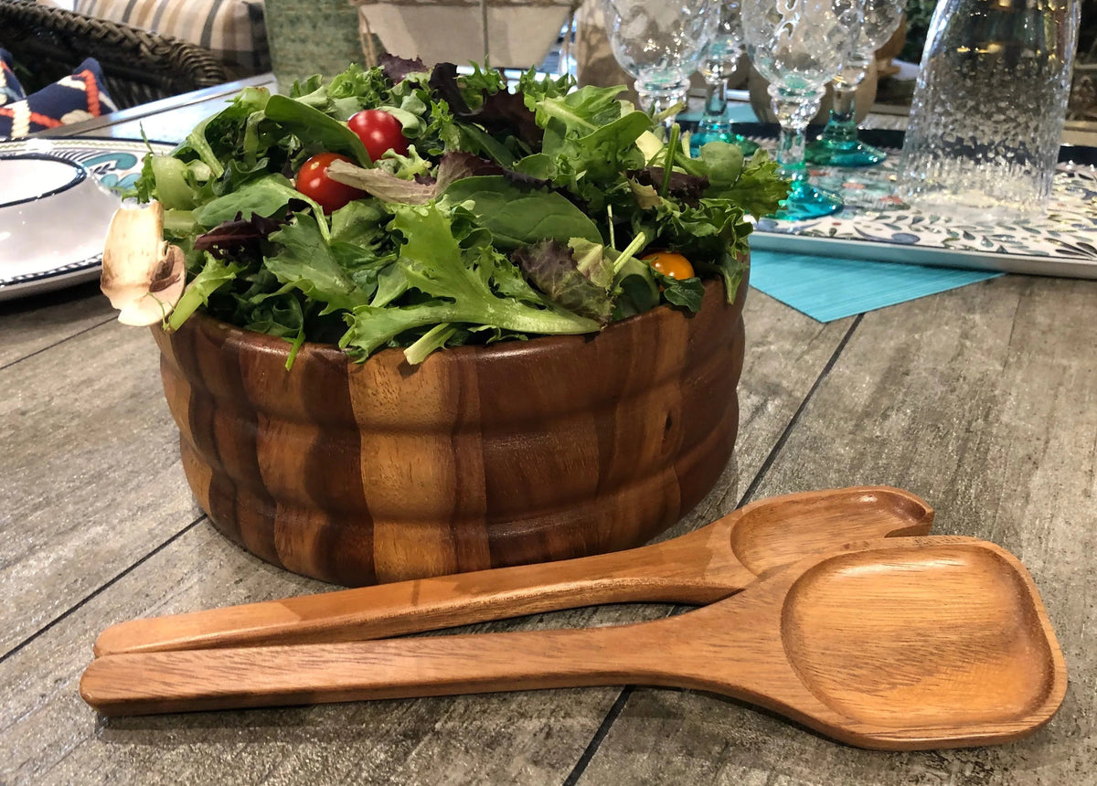 Wooden salad bowl filled with fresh salad, paired with matching wooden serving utensils.