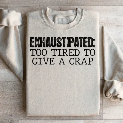 Sand-colored sweatshirt featuring peach text saying Exhaustipated To Tired To Give A Crap on front.