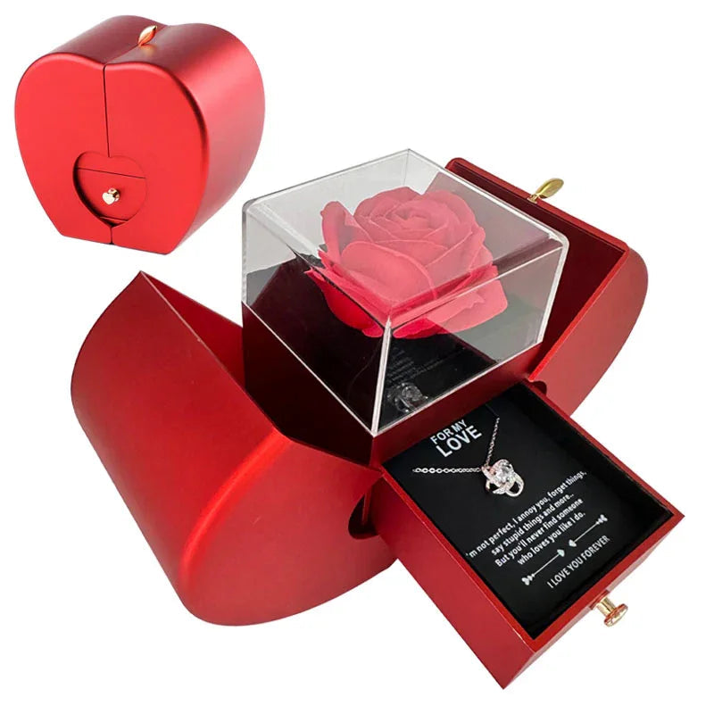 Red apple-shaped jewelry box with artificial rose inside on Christmas-themed background.