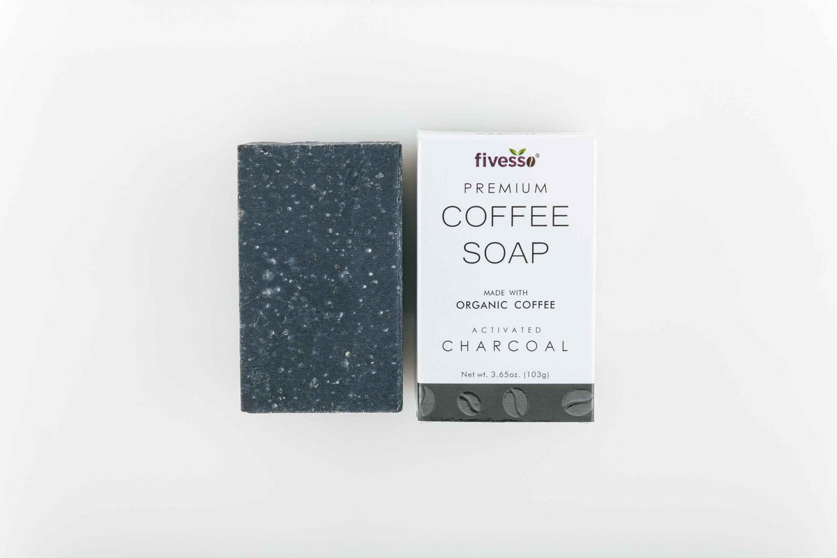 Close-up of charcoal coffee soap bar on a wooden surface with scattered coffee beans and a cloth background.