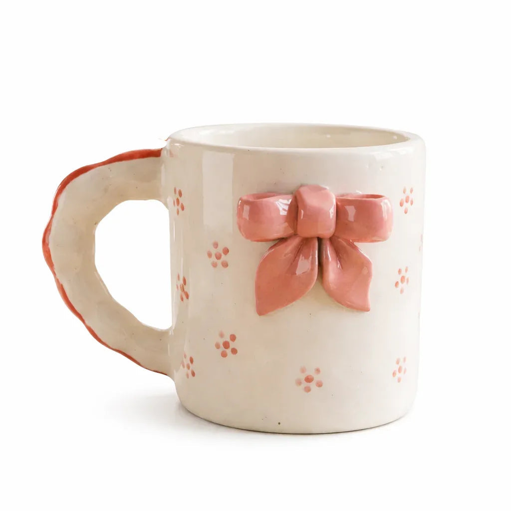 Handcrafted ceramic mug with a pink bow detail on a white background