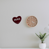 Hugs Candy Heart metal wall art hanging next to a clock on a gray wall