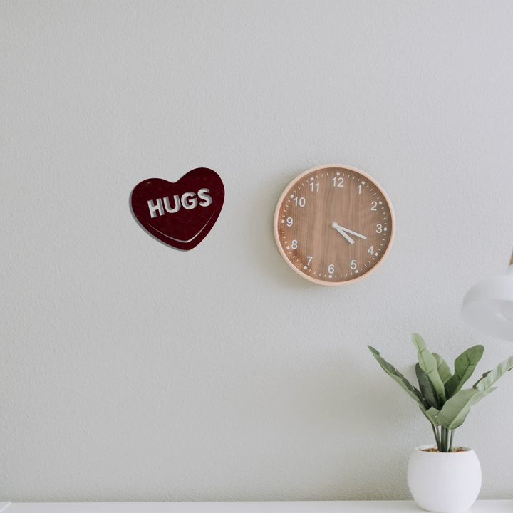 Hugs Candy Heart metal wall art hanging next to a clock on a gray wall