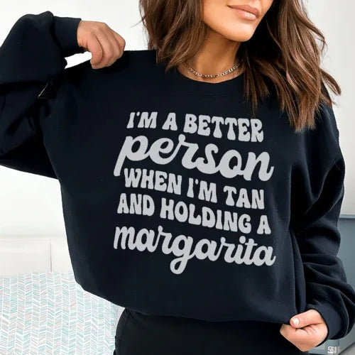 Black T-shirt front view displaying text 'I'm A Better Person When I'm Tan And Holding A Margarita' in peach.