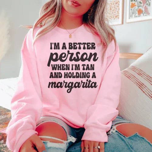 Light pink T-shirt with the printed phrase 'I'm A Better Person When I'm Tan And Holding A Margarita' in peach.