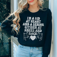 Black sweatshirt with 'I'm A Kid At Heart And A Senior Sitizen' text in white and peach fonts.