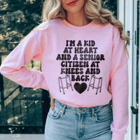 Light pink sweatshirt featuring 'I'm A Kid At Heart And A Senior Sitizen' text in white and peach colors.