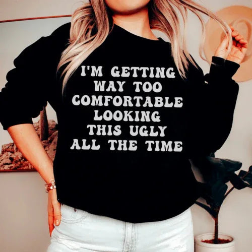 Black sweatshirt with white and pink text reading 'I'm Getting Way Too Comfortable Looking This Ugly All The Time'.