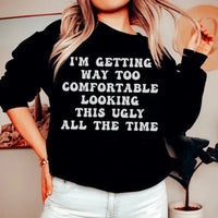 Black sweatshirt with white and pink text reading 'I'm Getting Way Too Comfortable Looking This Ugly All The Time'.