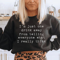 Peach-colored sweatshirt with text 'I'm Just One Drink Away' on front, cozy fleece fabric visible.