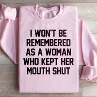 Light pink sweatshirt displaying the text 'I Won't Be Remembered As A Woman Who Kept Her Mouth Shut' in white letters.