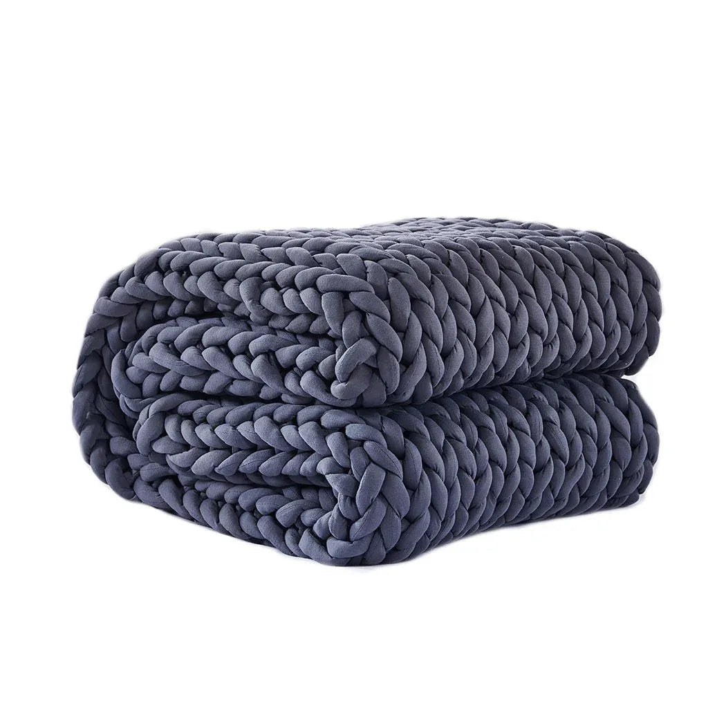 Chunky bulky knit throw blanket in soft beige spread on a bed showing its thick texture.