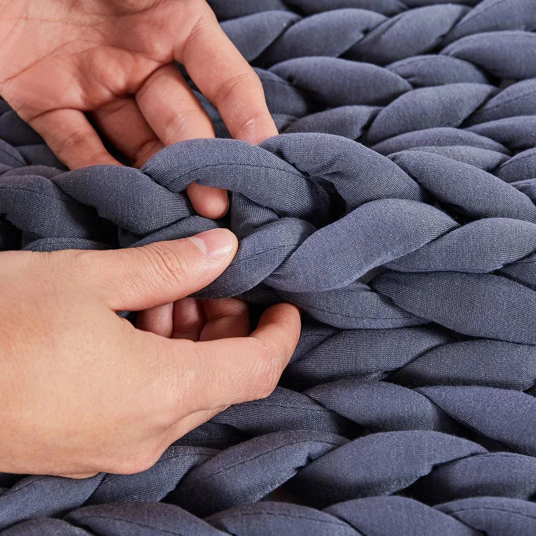 Weighted chunky knit blanket in creamy color arranged on a neutral background to showcase design.