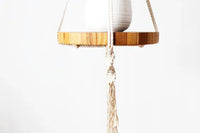 Close-up view of detailed knots and woven pattern of macrame plant hanger with wooden tray below pot.