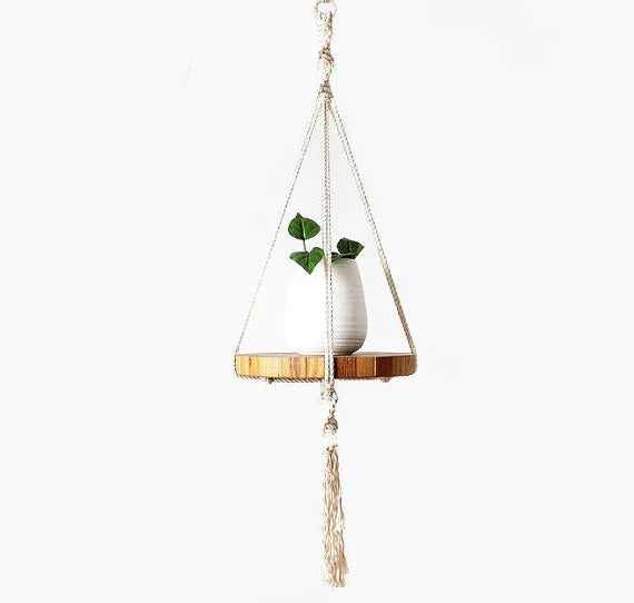 Handcrafted ecru cotton macrame plant hanger with wooden tray, hanging against white wall