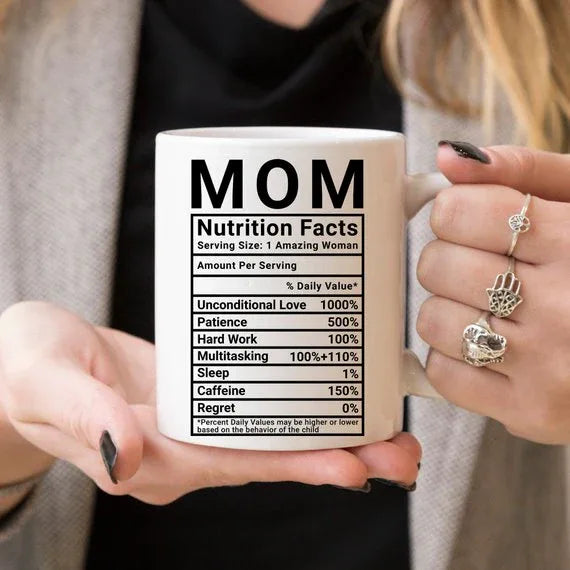 Top angle of white ceramic mug with black printed nutrition facts for moms, on a wooden table.