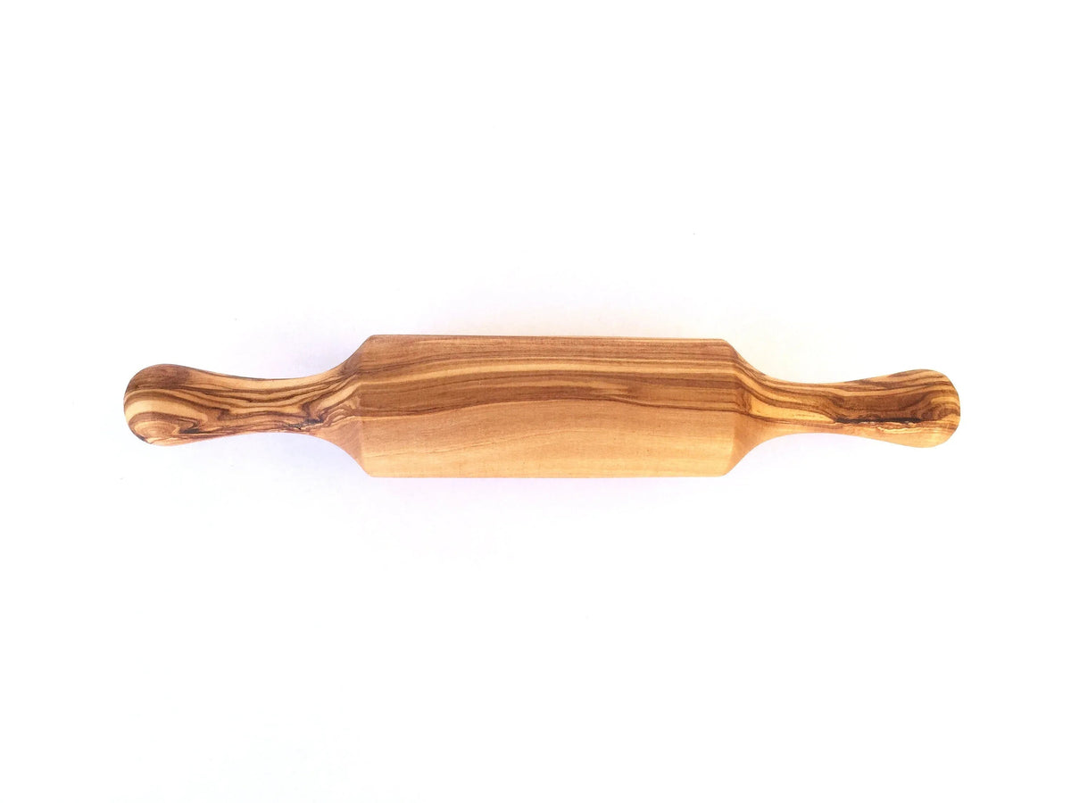 Mini rolling pin placed on a wooden cutting board alongside cookie dough and baking tools.