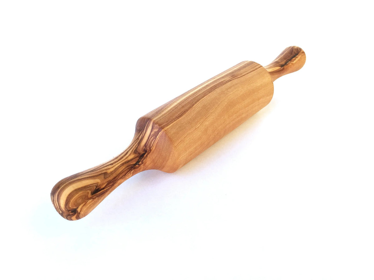 Child’s hands holding the mini rolling pin with two handles over dough for baking pizza or cookies.