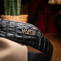 Man adjusting black caiman belt while wearing denim and casual shirt