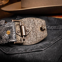 Close-up of gray crocodile belt worn with brown leather watch and jeans.