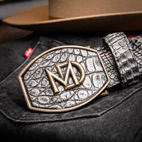 Individual adjusting gray caiman crocodile belt over blue denim pants.