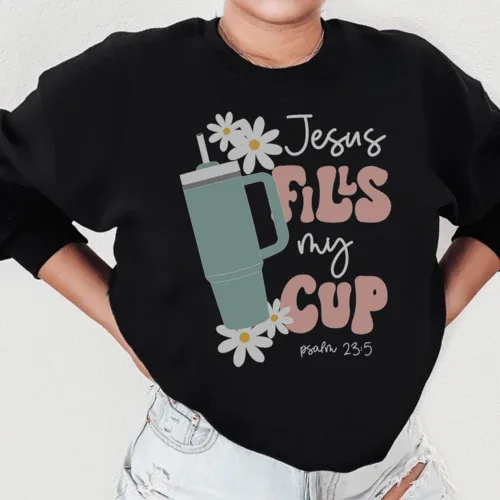 Black sweatshirt showing "Jesus Fills My Cup Psalm" text design, displayed on a flat surface.