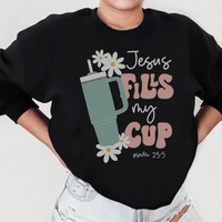 Black sweatshirt showing "Jesus Fills My Cup Psalm" text design, displayed on a flat surface.