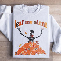 White sweatshirt with a stylized autumn leaf design in orange and yellow accompanied by Leaf Me Alone Fall text