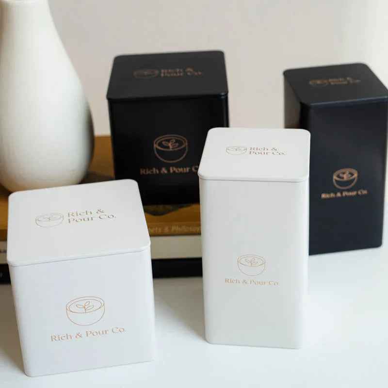 Close-up of three pastel-colored tea tins arranged in a neat row on a dark wooden table.