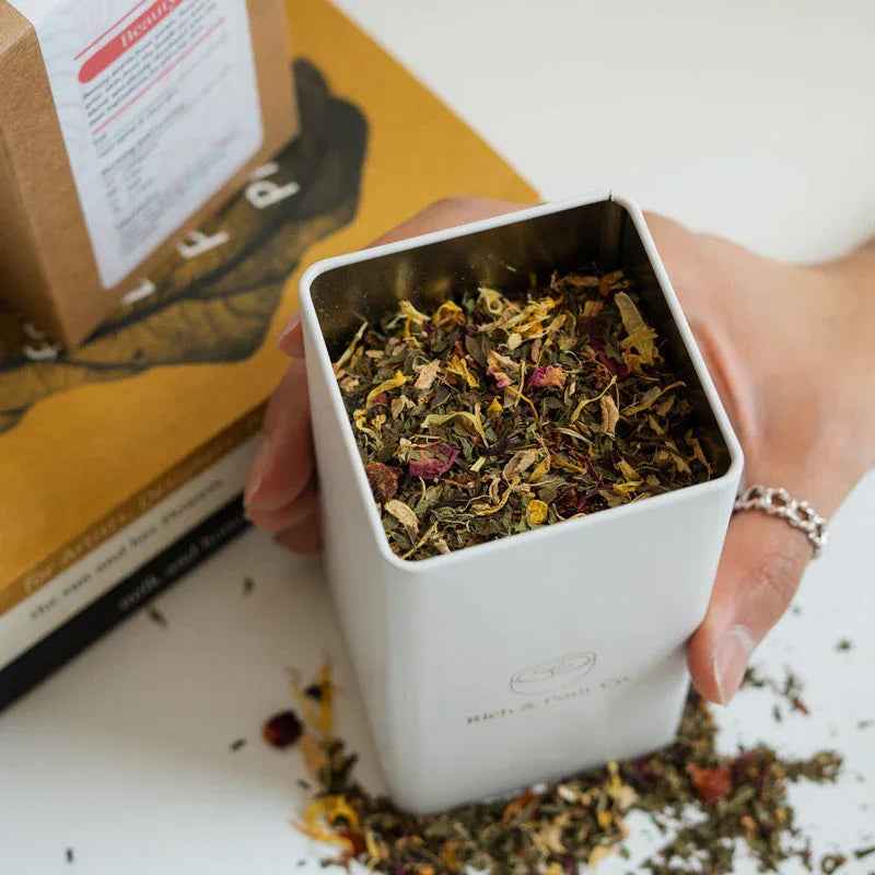 Three colorful tea storage tins stacked on a wooden surface with greenery background.