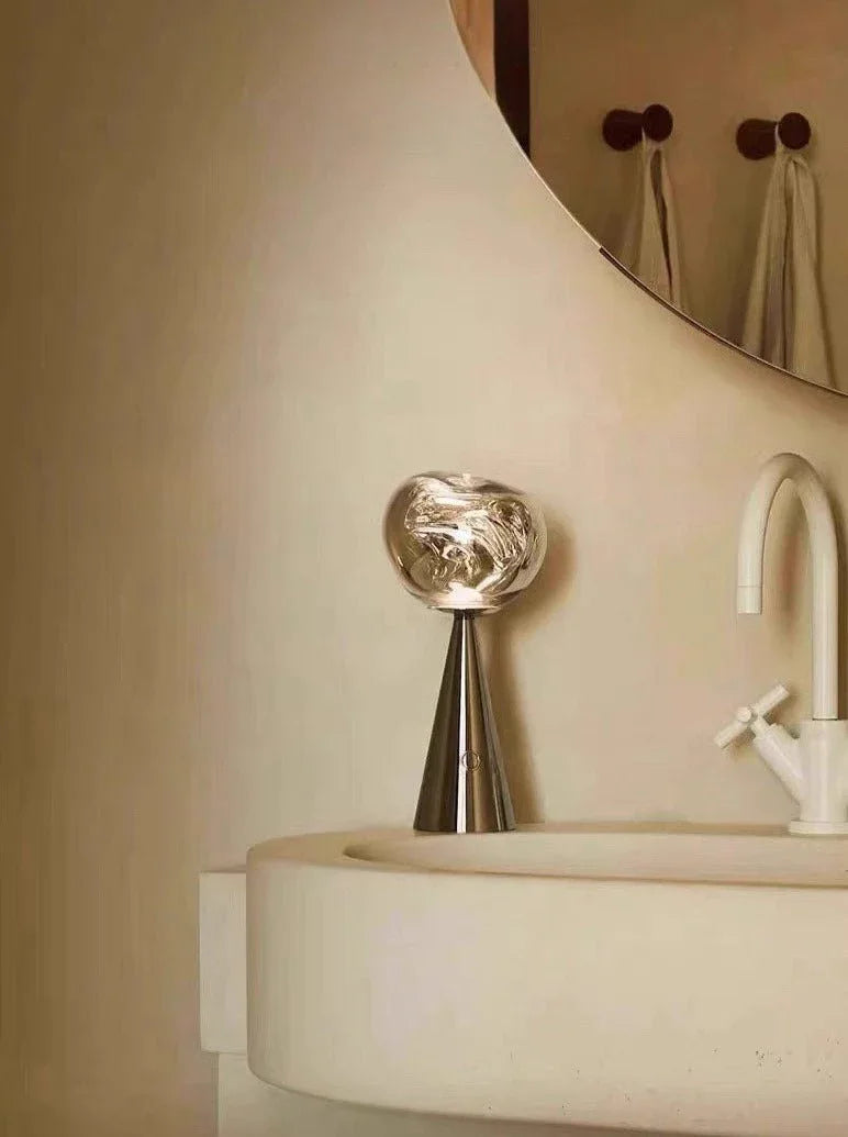 Hand holding a compact portable table lamp with dimmable warm LED light in a bedroom.