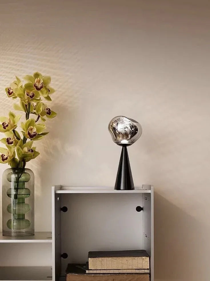 Close-up of a small modern table lamp with a melting glass design emitting soft warm light.