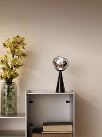Close-up of a small modern table lamp with a melting glass design emitting soft warm light.