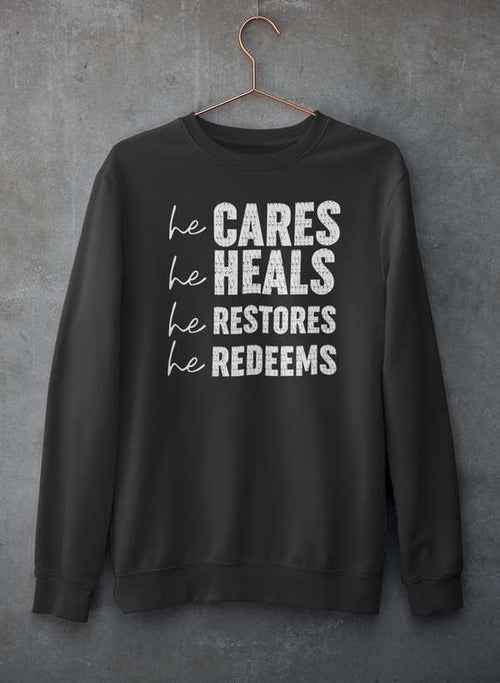 Gray sweatshirt with text He Cares He Heals He Restores He Redeems on front hanging on a hanger.