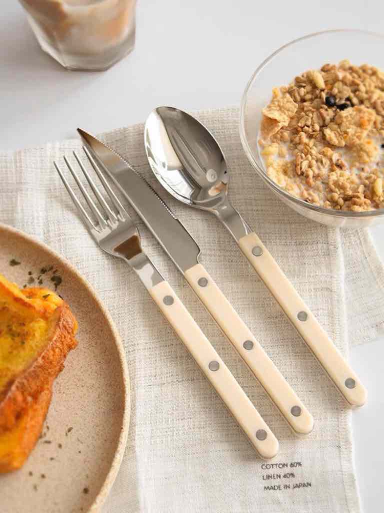 Close-up of stainless steel flatware pieces with smooth ivory-colored handles arranged on a light background.