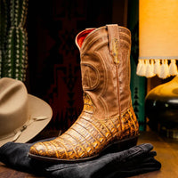Side view of man walking in mustard brown caiman cowboy boots paired with rolled jeans outdoors.