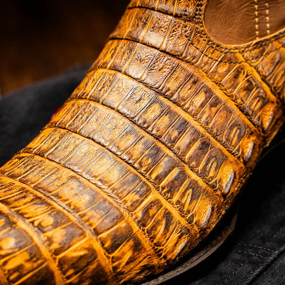Lifestyle shot of cowboy boots in mustard brown caiman leather worn with casual outfit.
