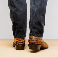 Man standing with feet crossed wearing genuine caiman belly skin cowboy boots in mustard brown.