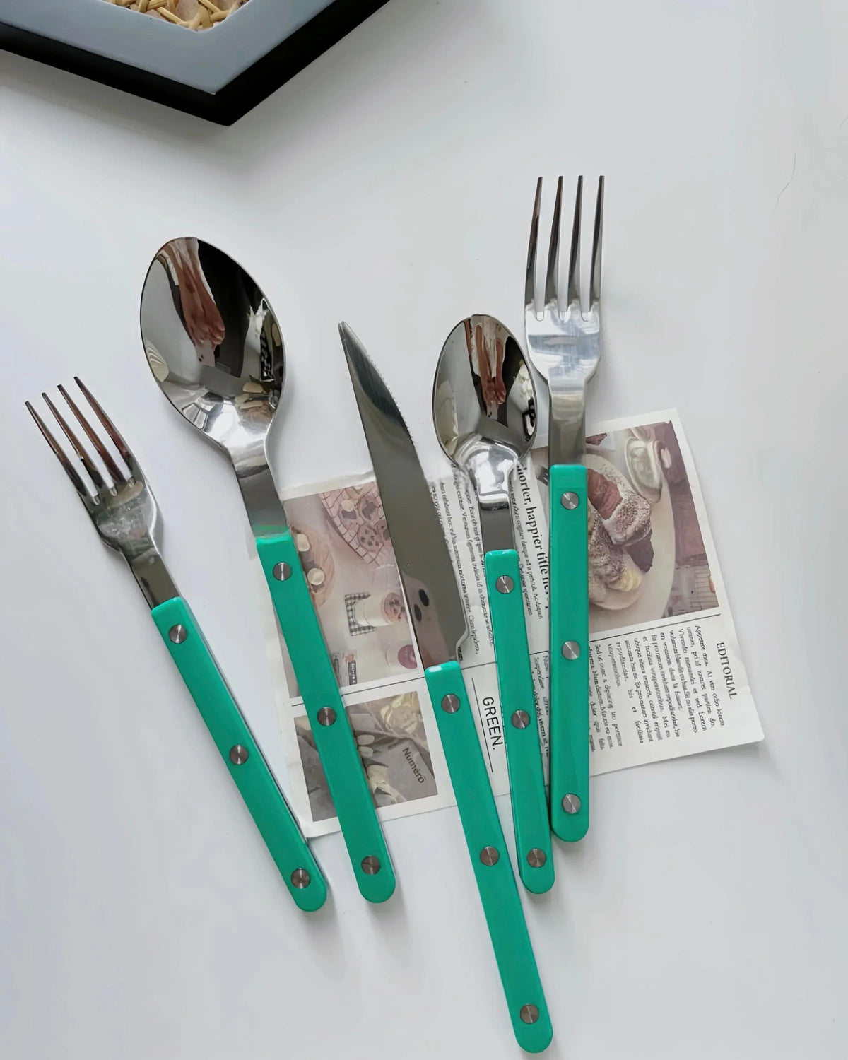 Close-up of turquoise modern French rivet cutlery with sleek handles on a kitchen table.